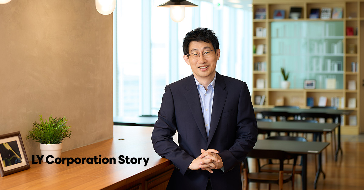 The CPO, Shin, dressed in a suit, is standing indoors with a gentle smile. In the background, there is a bookshelf and a table, creating a calm and composed atmosphere. The text 