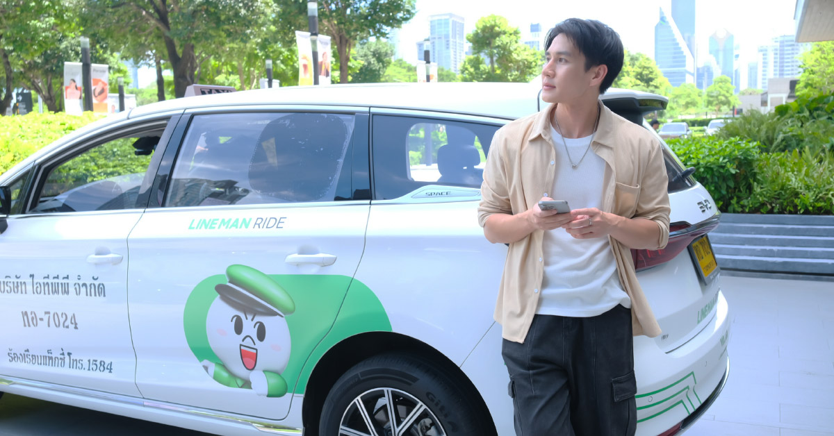 A person stands beside a ride-hailing vehicle while holding a smartphone.