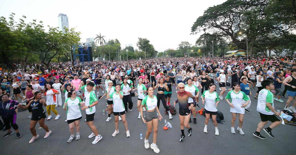 Thousands of participants take part in an outdoor fitness event, exercising together on a city street.