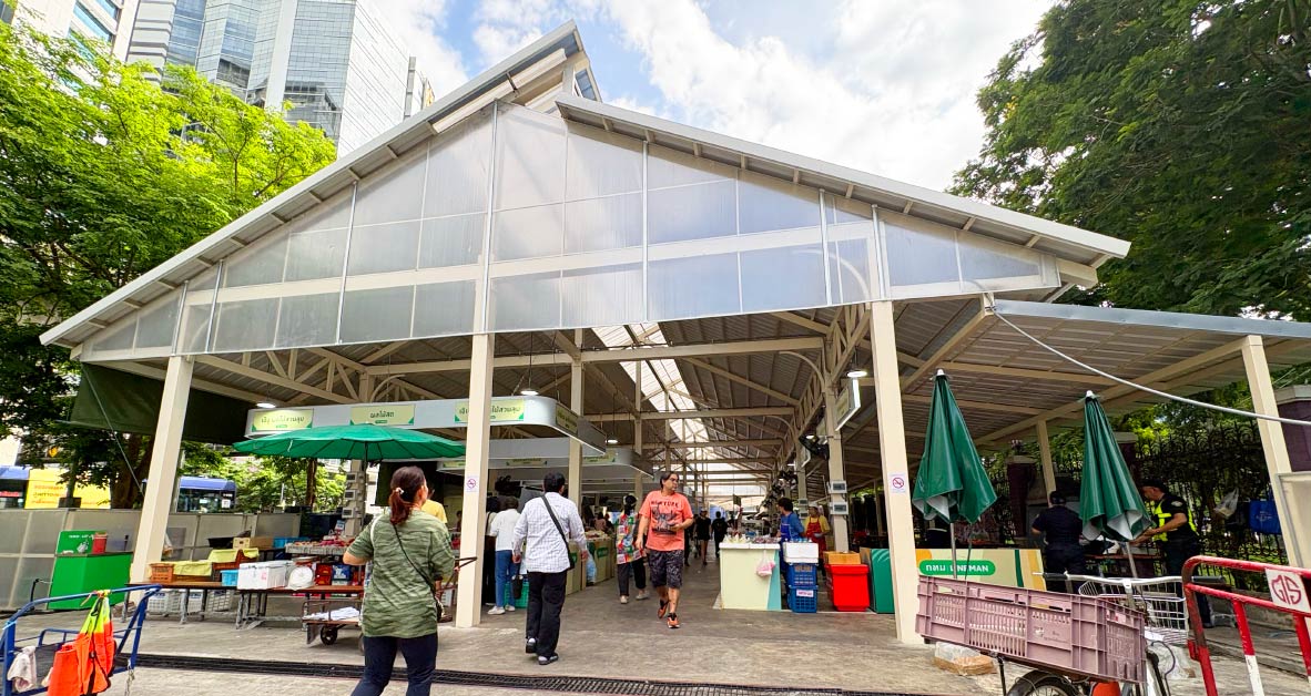The entrance to an open-air market with a large white roof covering rows of stalls.
