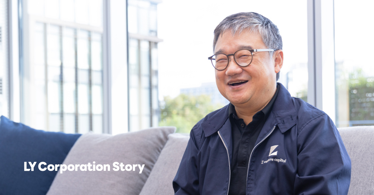 A man seated on a sofa, CEO Fan, is smiling and looking toward the camera. He has short gray hair and wears round glasses and a navy jacket. Buildings can be seen through the large window in the background, and the words LINE Yahoo Story appear in white text at the lower left of the screen.