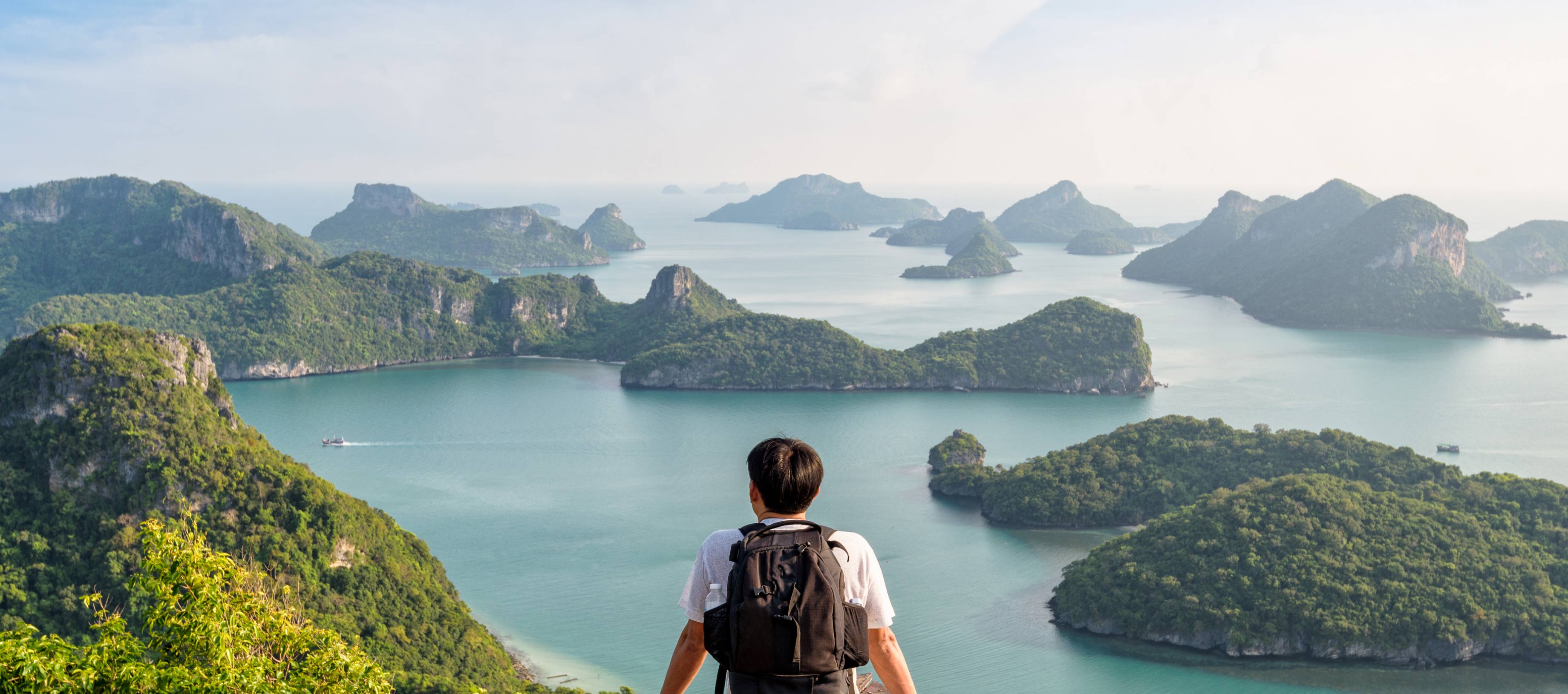 目の前に広がる青い海と島々の絶景を、高台からリュックを背負って見つめる男性の背中。中央にはLINEヤフーのミッション「WOW Our Users!」のテキストが配置されています。
