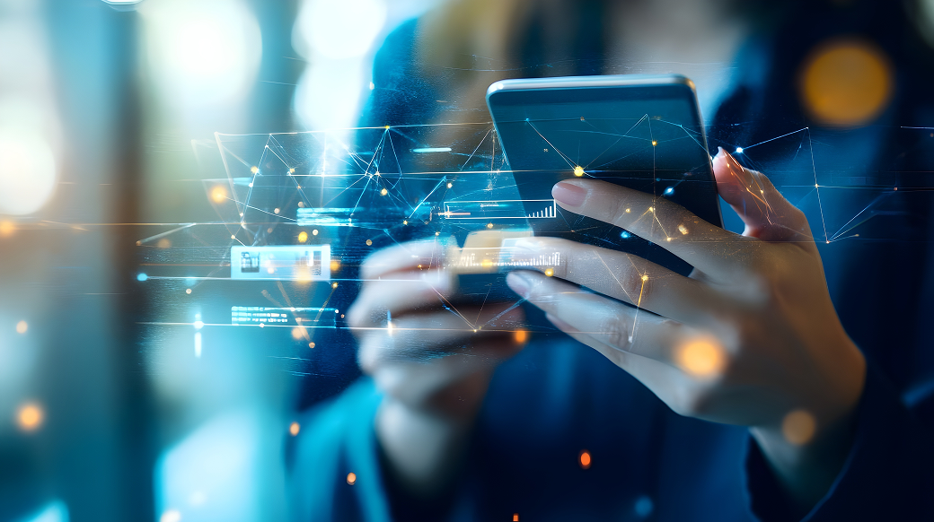 スマートフォンを持つ人物の手元が写っており、そこにデジタルデータのような光の線やグラフ、ネットワークを示すアイコンが重なって描かれているイメージ画像。青やオレンジの光が散りばめられ、未来的でサイバーな雰囲気が強調されている。