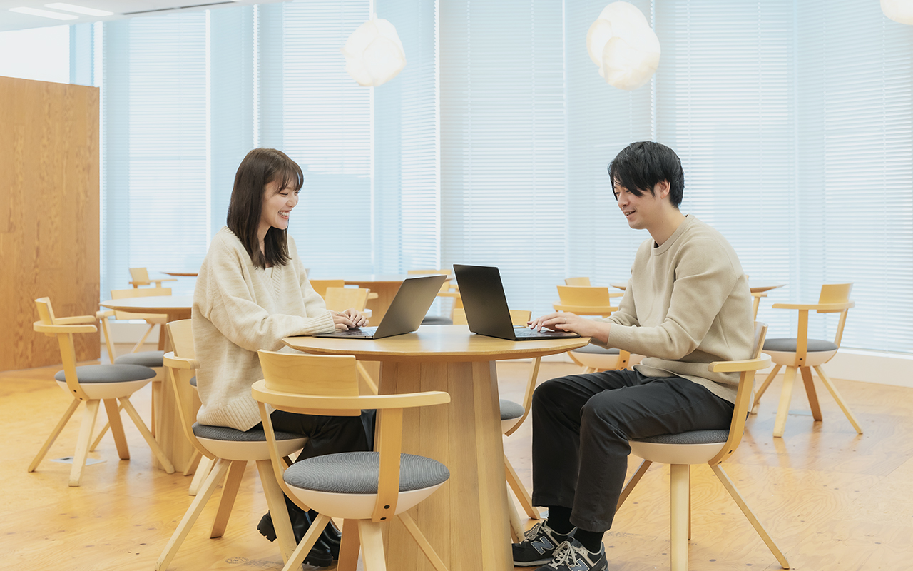明るいオフィスのラウンジで、リラックスしながらノートPCで作業する2人