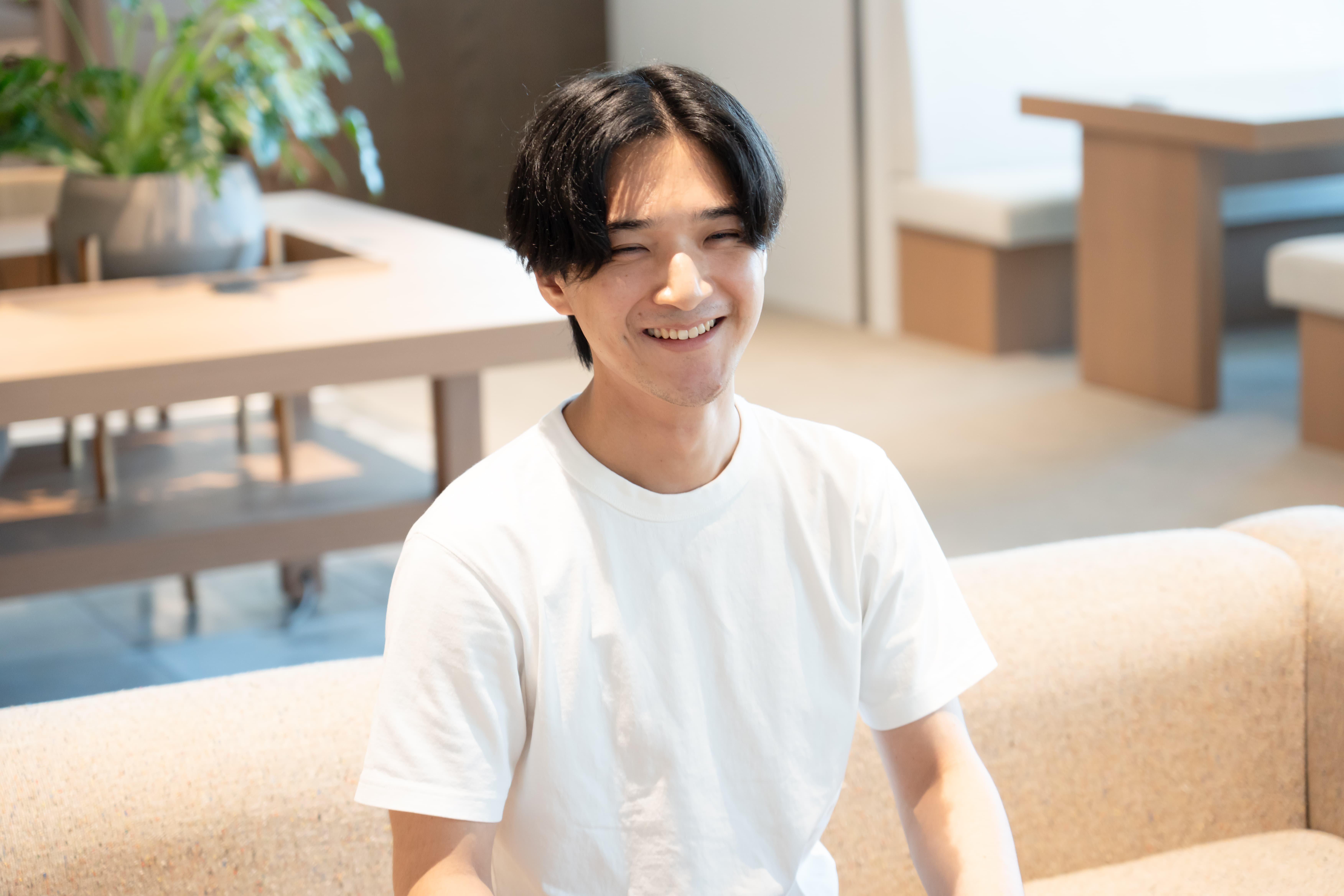 ソファに座って笑顔を見せる中野修平さんの写真。