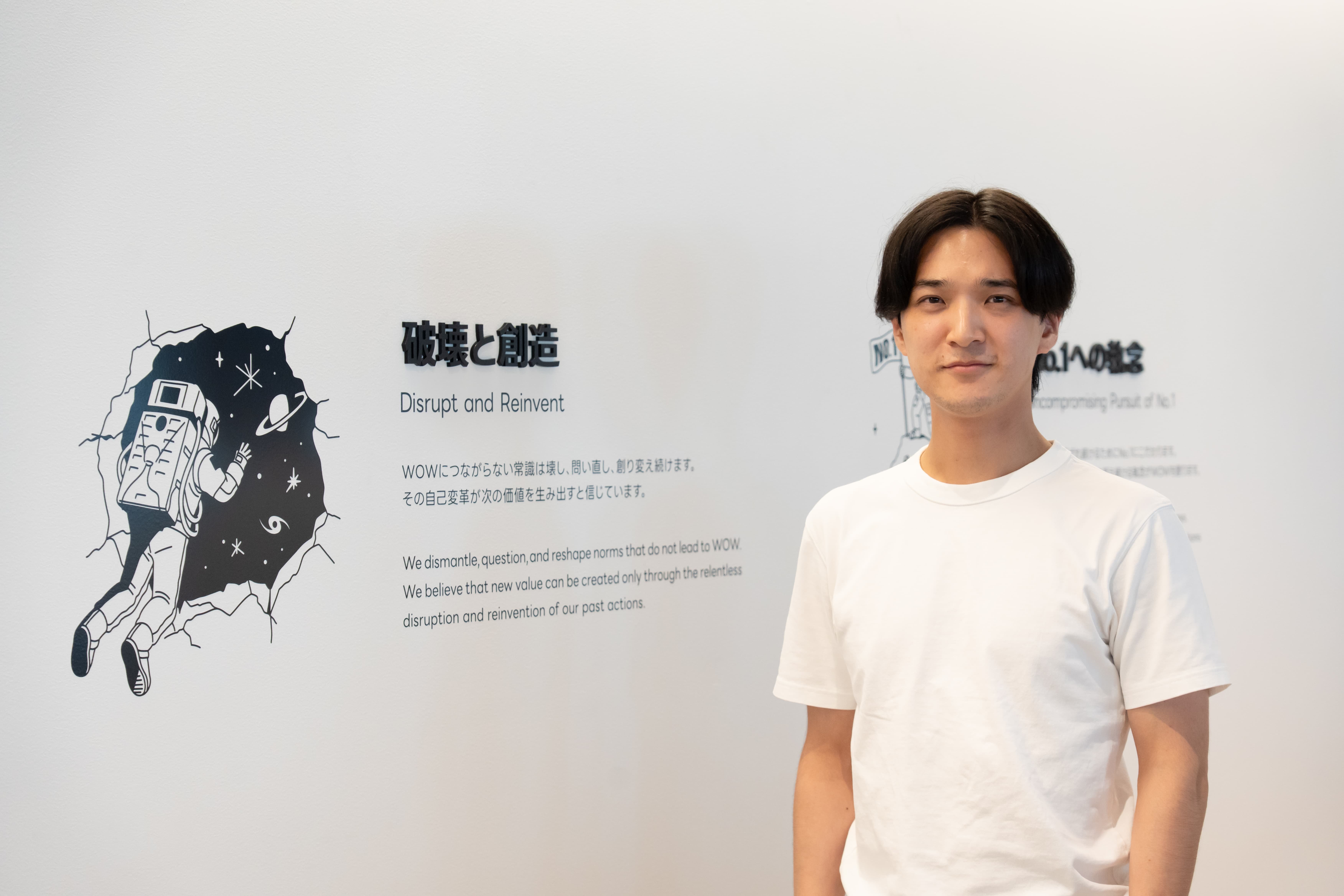 破壊と創造のメッセージが掲示された壁の前に立つ中野修平さんの写真。