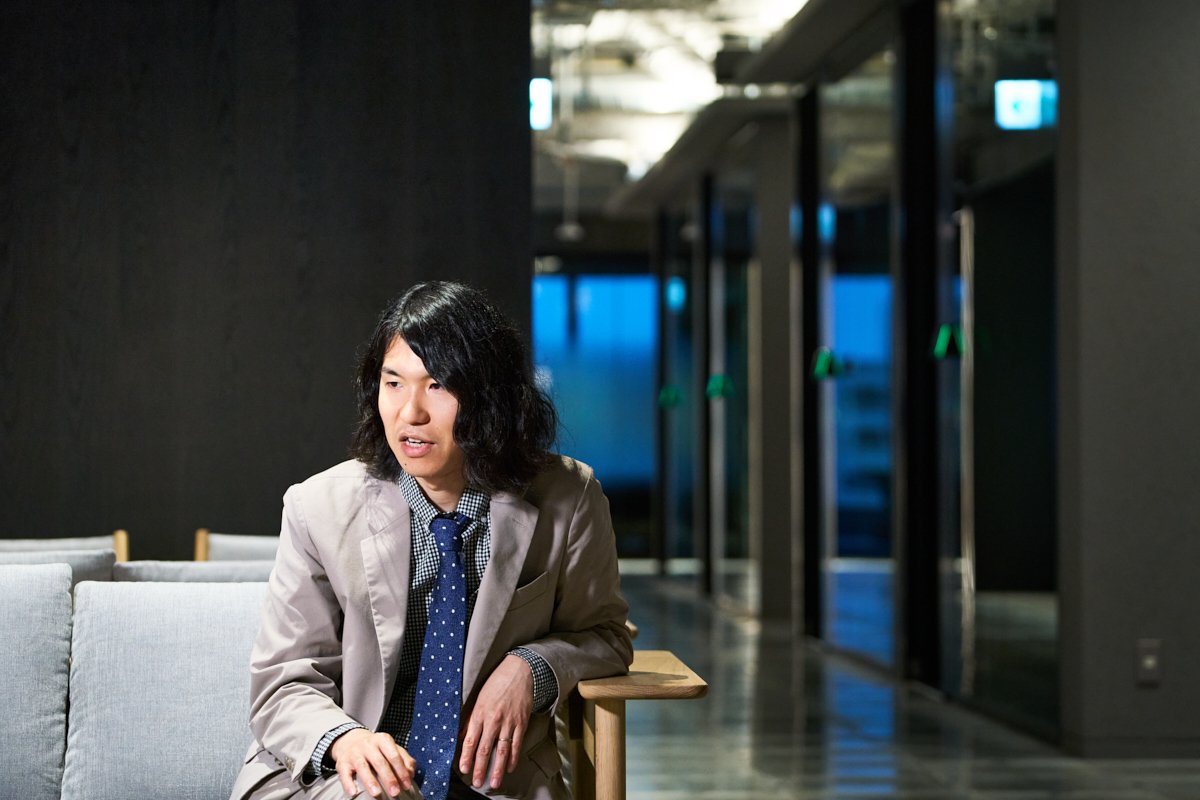 ソファに座った樋口恭介さんが廊下を背景にインタビューに応じている写真。