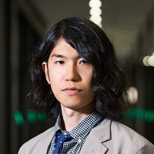 黒髪の樋口恭介さんが廊下のような空間に立ち、カメラに向かって静かな表情を見せている写真。