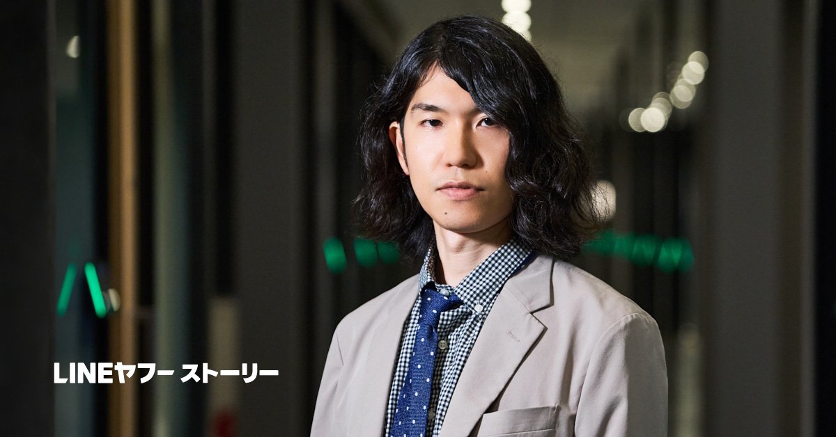 黒髪の樋口恭介さんが廊下のような空間に立ち、カメラに向かって静かな表情を見せている写真。