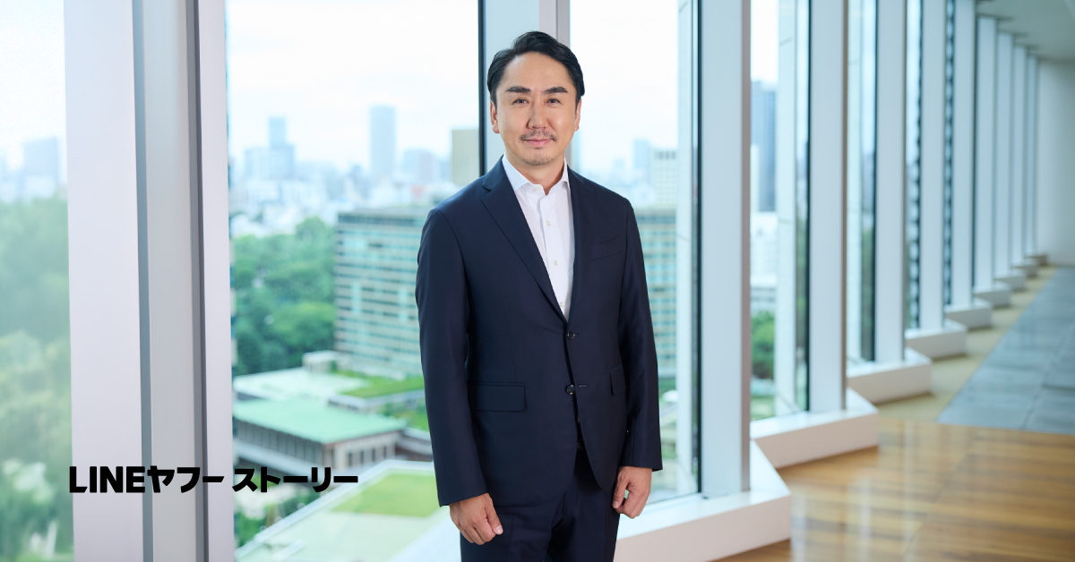 室内でスーツを着たCPOの慎が微笑んで立っています。背景には本棚やテーブルがあり、落ち着いた雰囲気です。「LINEヤフー ストーリー」という文字が左下に表示されています