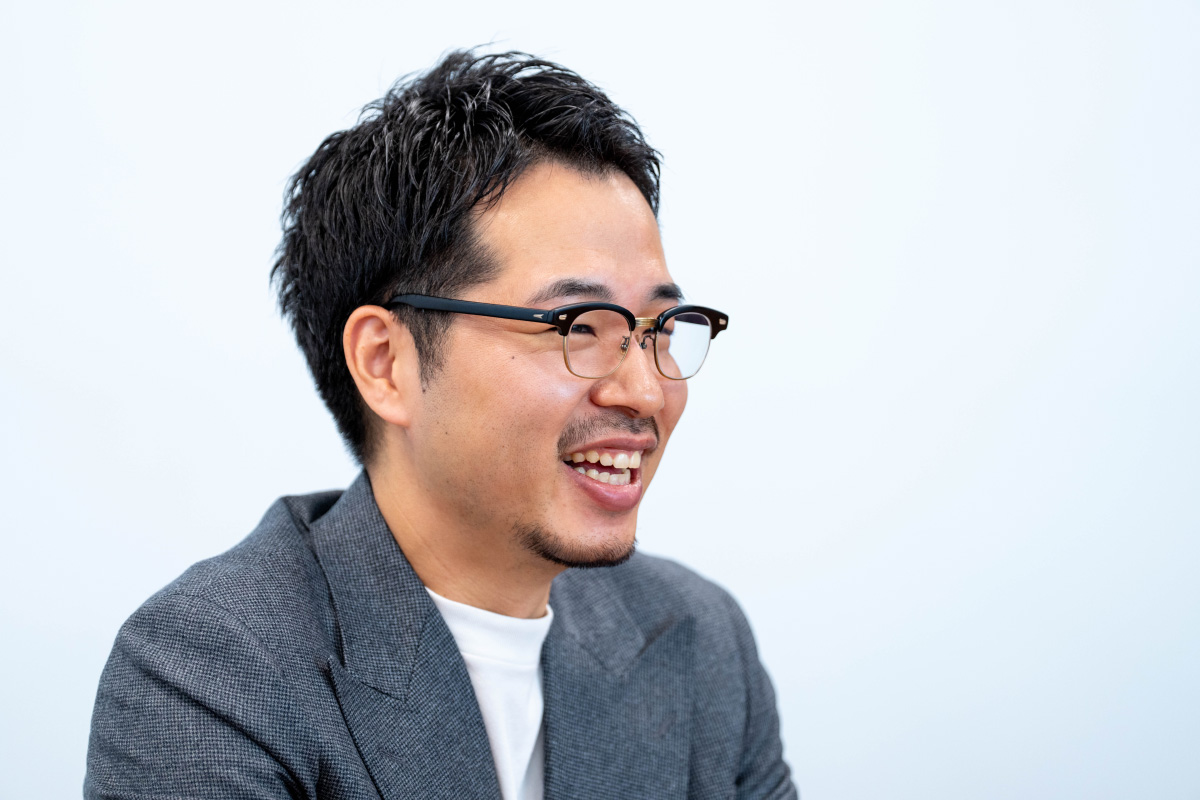 二木さんのバストショットです。横向きに座りながら口を開けて笑っている。視線は正面ではなくやや右方向に向けられ、会話中の一瞬を捉えたような自然な表情。