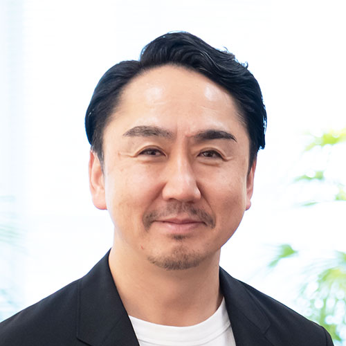 黒ジャケットのCEO出澤の顔のクローズアップ。短く整えた黒髪とあごひげが特徴で、穏やかな表情でカメラを見ている