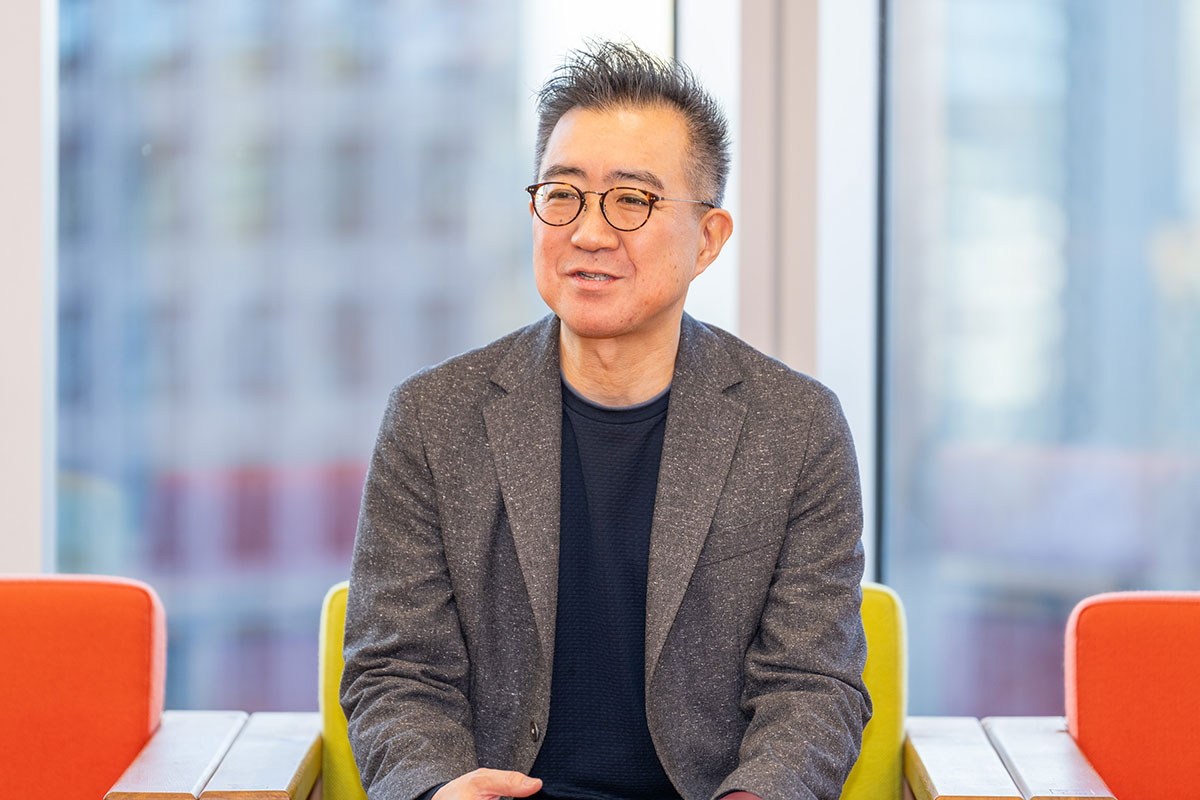 メガネをかけた兵頭CEOがカラフルな椅子に座り、リラックスした様子で話しています。背景に窓があります