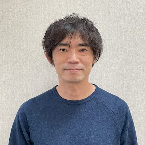 青い服を着た男性、柿崎が笑顔で写っています。