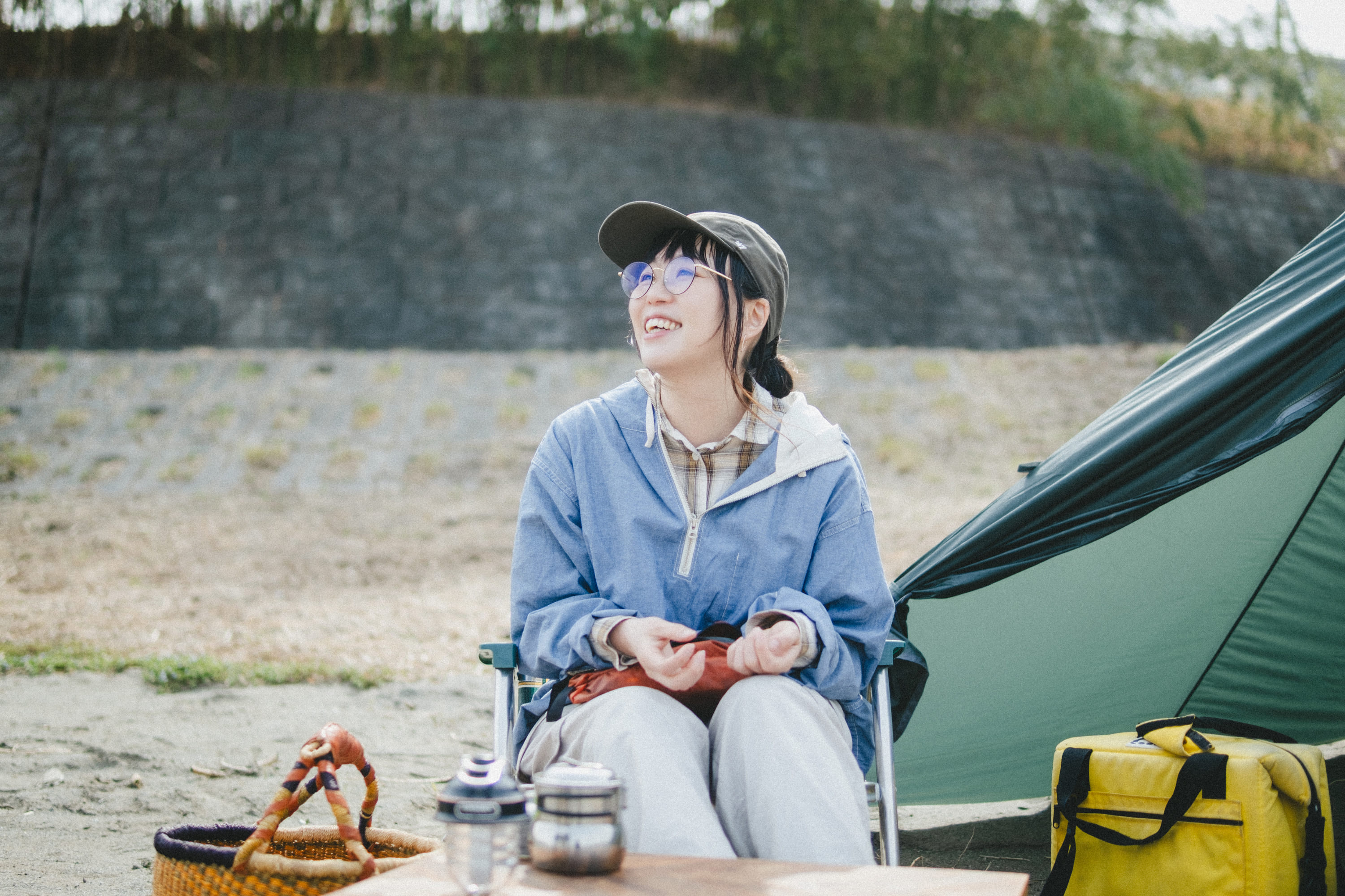 屋外のキャンプ場で、テントの横に置かれたアウトドアチェアに座るこいしさんの写真。