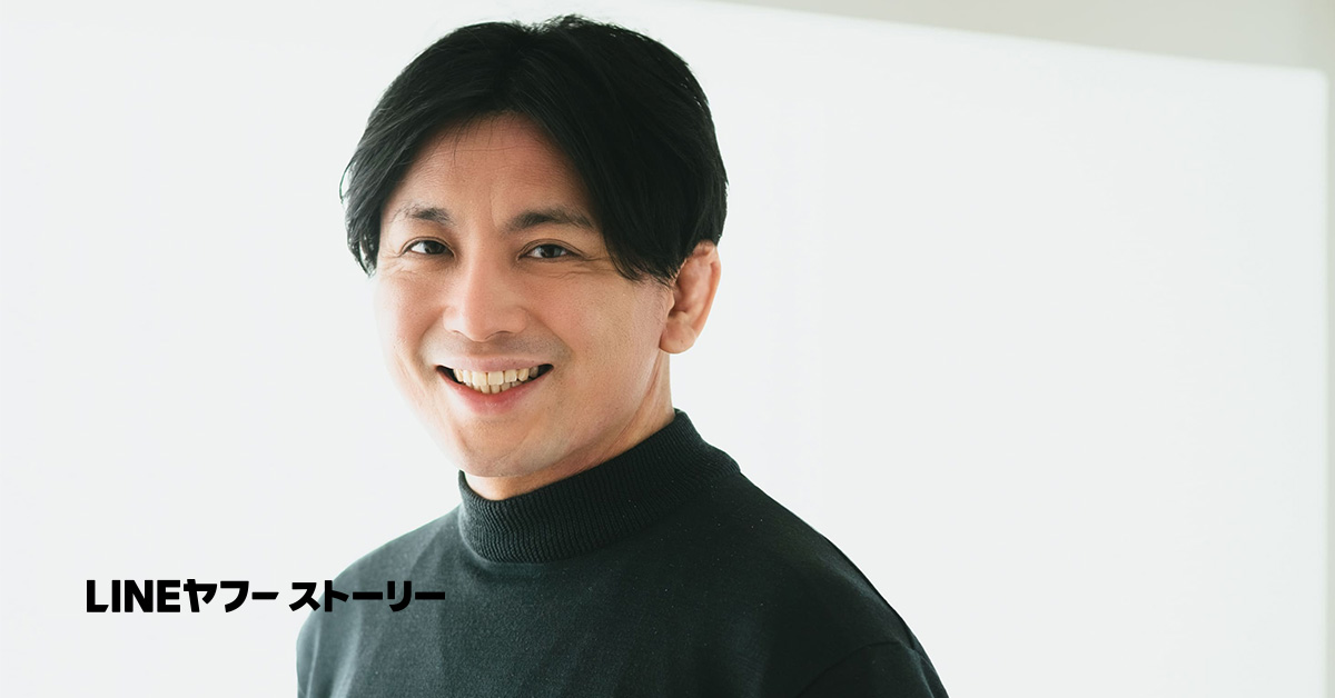 益田さんのバストショット。黒のタートルネックを着用し、黒髪を中央で分けて自然に流した髪型をしている。白い背景の前でやや斜めに体を向け、穏やかな笑顔でカメラを見つめている。