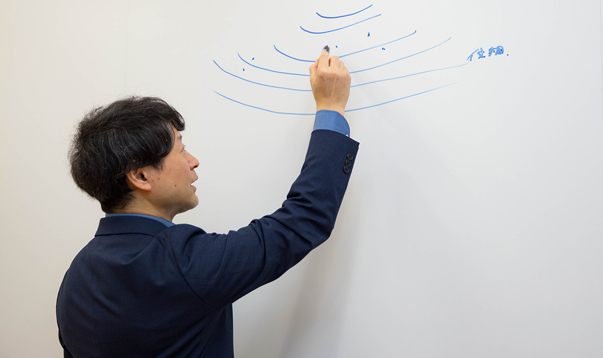 浦崎が白いホワイトボードに青いマーカーで線を描いている。