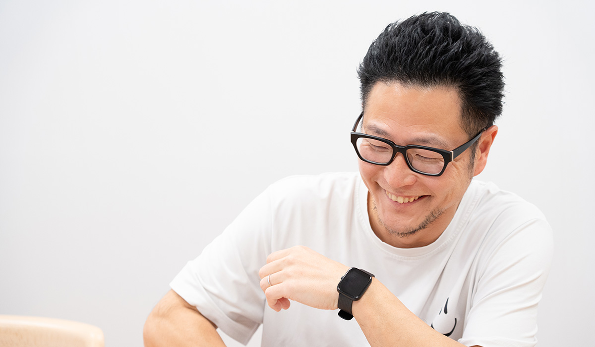 男性が笑顔で座っており、腕時計をしています。リラックスした雰囲気です。