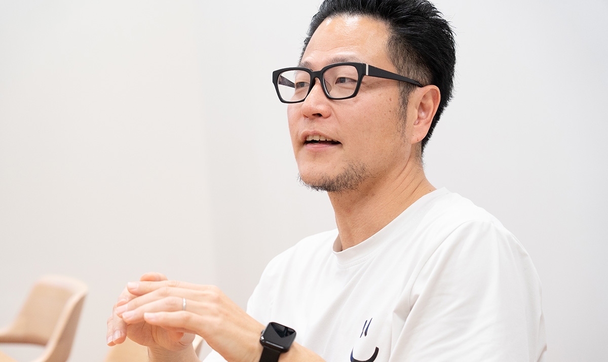 男性が話をしている様子で、手を組みながら説明しています。