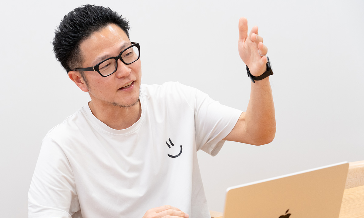 男性が手を上げて説明している様子です。前にノートパソコンが置かれています。