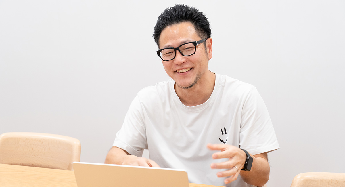 男性が笑顔でパソコンを前にして座っています。リラックスした雰囲気です。