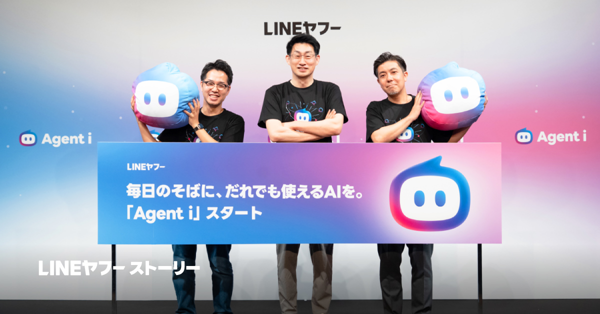 3人の男性が横一列に立ち、横長のパネルを持っている写真。背景には「LINEヤフー」と書かれており、パネルには「毎日のそばに、だれでも使えるAIを。『Agent i』スタート」と大きく記載され、右側に青とピンクのグラデーションで描かれた丸みのあるロボット風キャラクターのアイコンが配置されている。