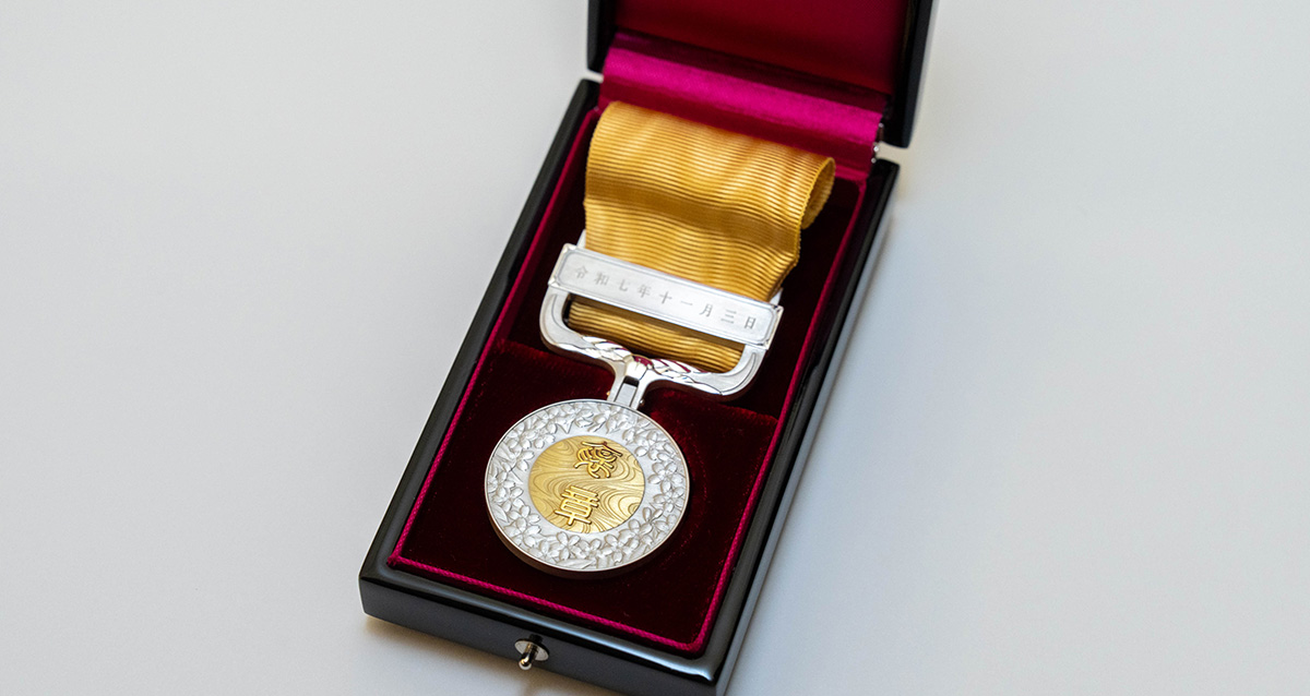 赤い内張りの黒いケースの中に、黄色いリボンが付いた銀と金のメダルが収められている。メダルには「黄綬」と刻まれており、リボンの金具部分には「令和七年十一月三日」と刻印されている。