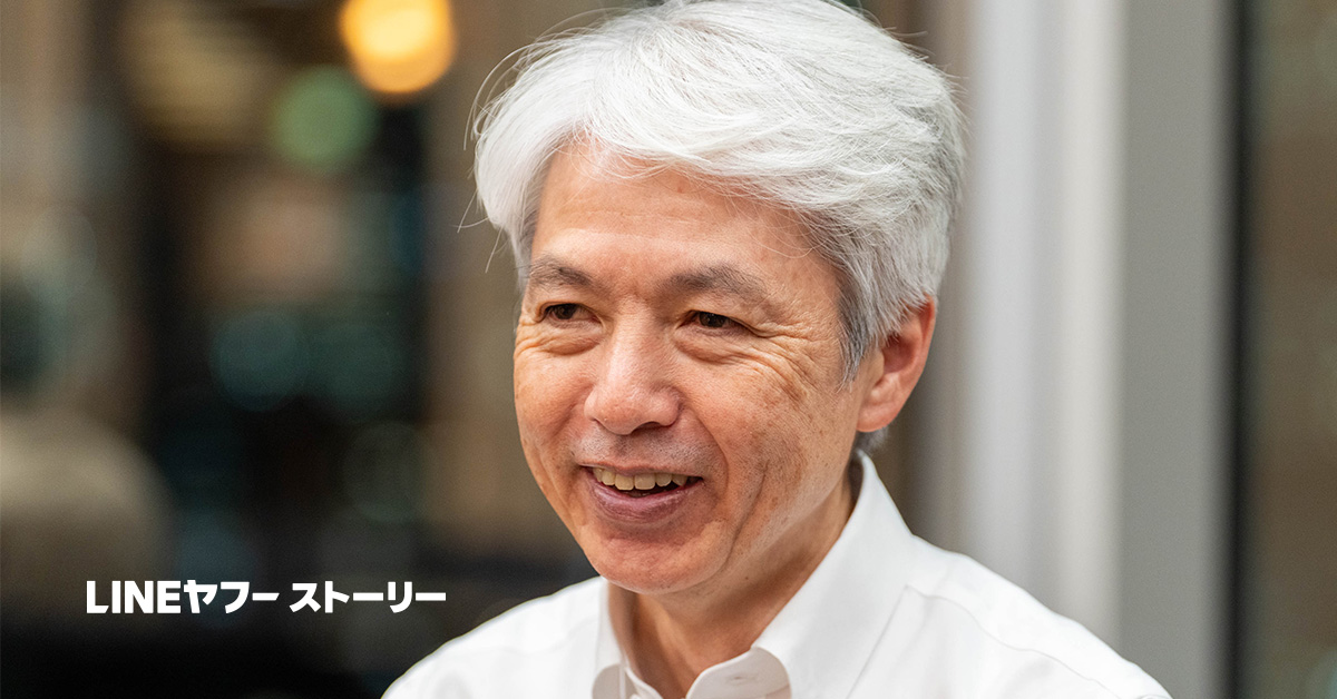 岩崎の写真。白髪のショートヘアで、白いワイシャツを着ている。