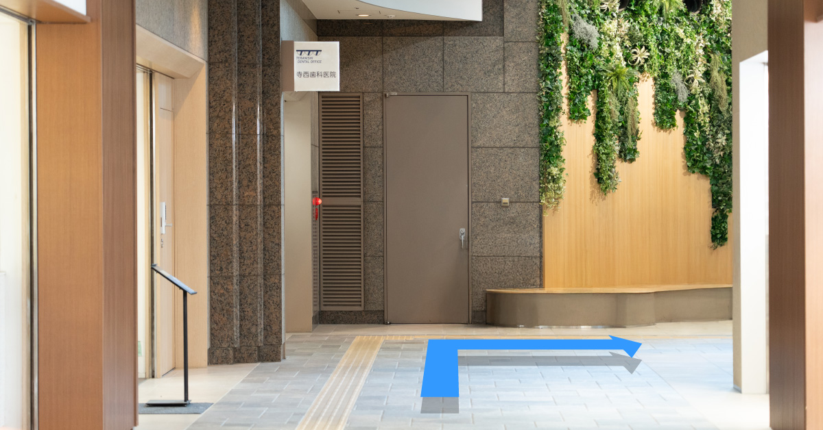 通路の突き当たりで右折する案内。床の青い矢印が進行方向を示し、右側の通路へ誘導する
