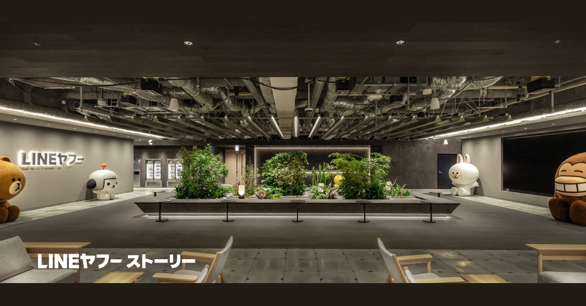 LINEヤフーのオフィスロビー写真。中央に緑豊かな植栽スペースがあり、左右にLINEキャラクターの大型オブジェが配置。「LINEヤフーストーリー」の文字表示あり