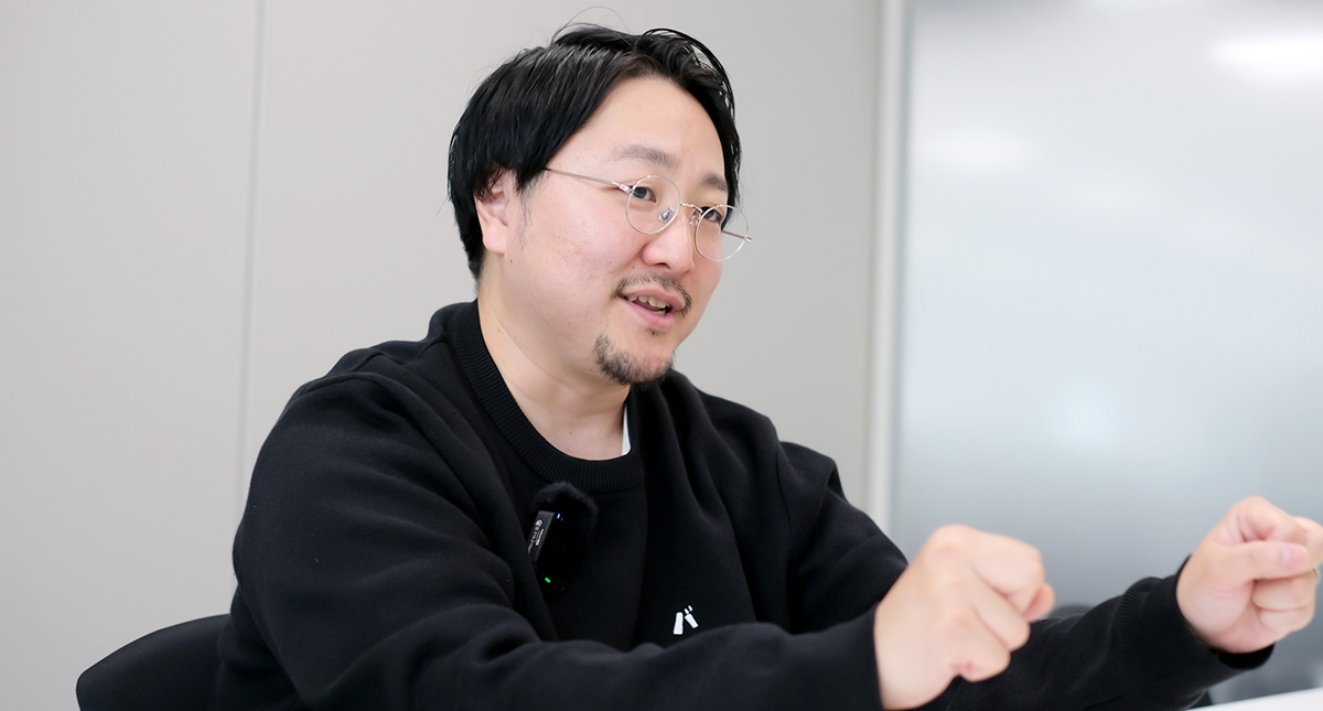 佐藤が体をやや前に傾けながら両手を前方に突き出し、何かを握るような仕草をして説明している様子
