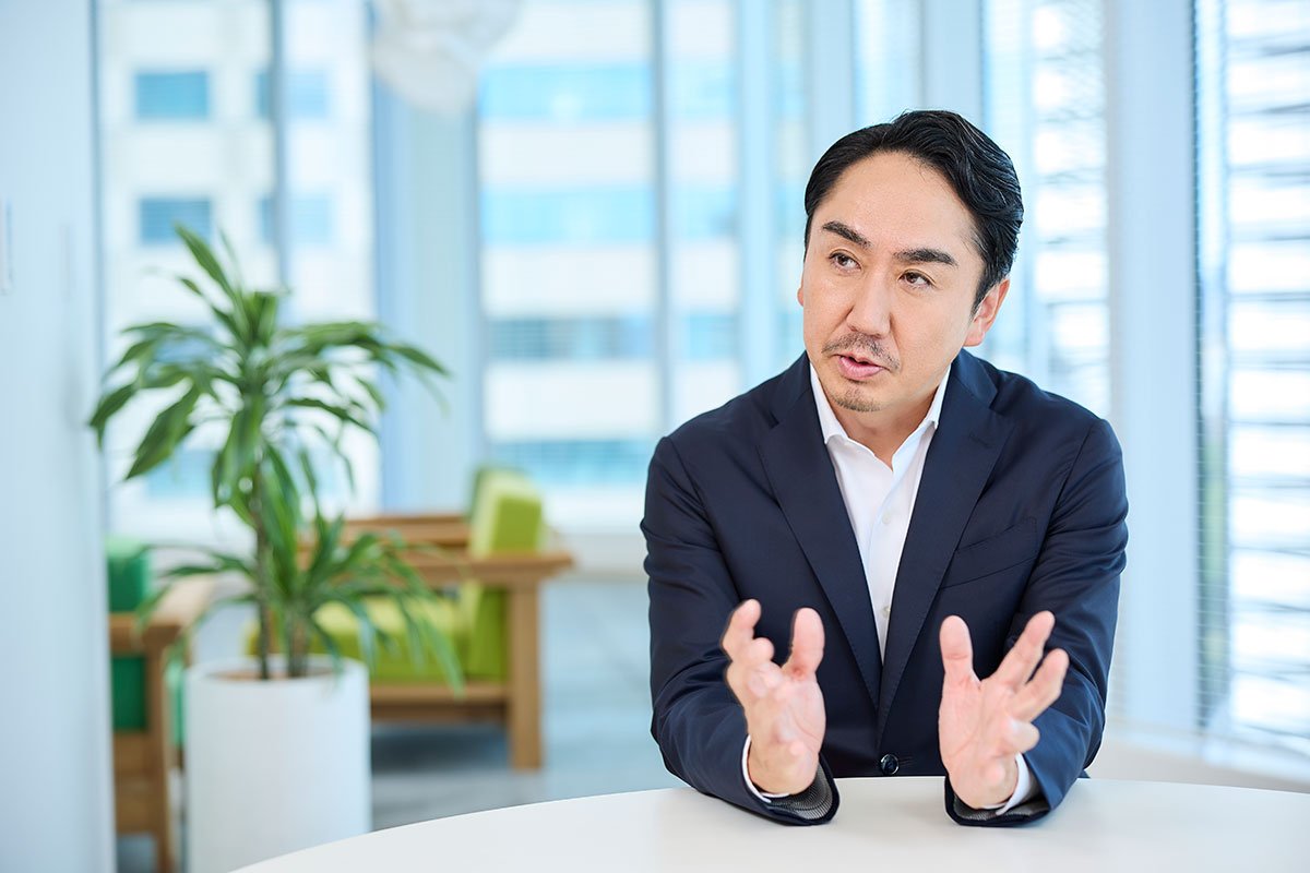 スーツ姿のCEO出澤が、テーブル越しに両手を広げながら話している写真