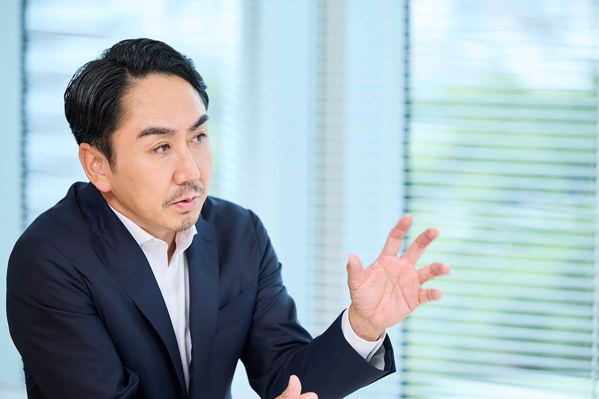 スーツ姿のCEO出澤が、片手を上げながら話している写真