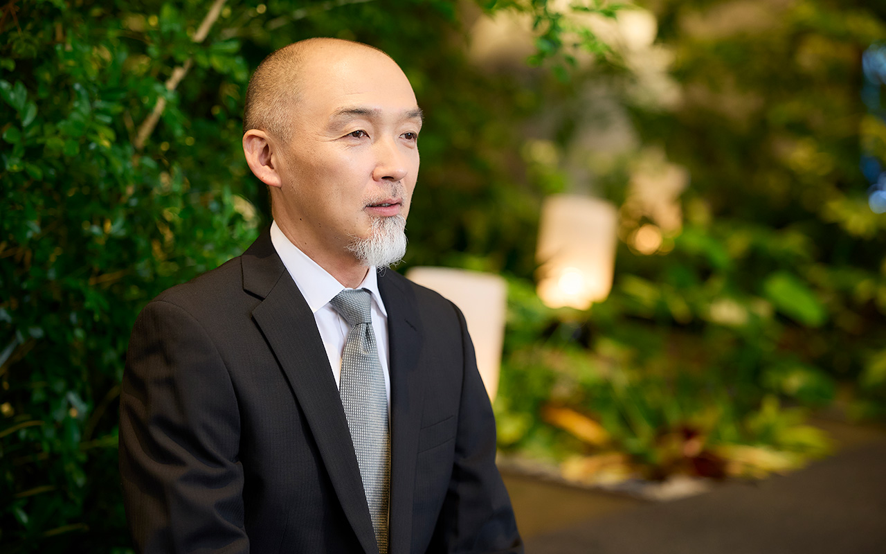 鈴木が落ち着いた姿勢で前方を見ながら話している様子