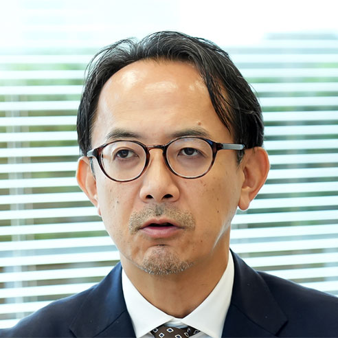 メガネをかけた川邊が話しています。背景にはブラインドがあり、真剣な表情で議論に参加しているように見えます。