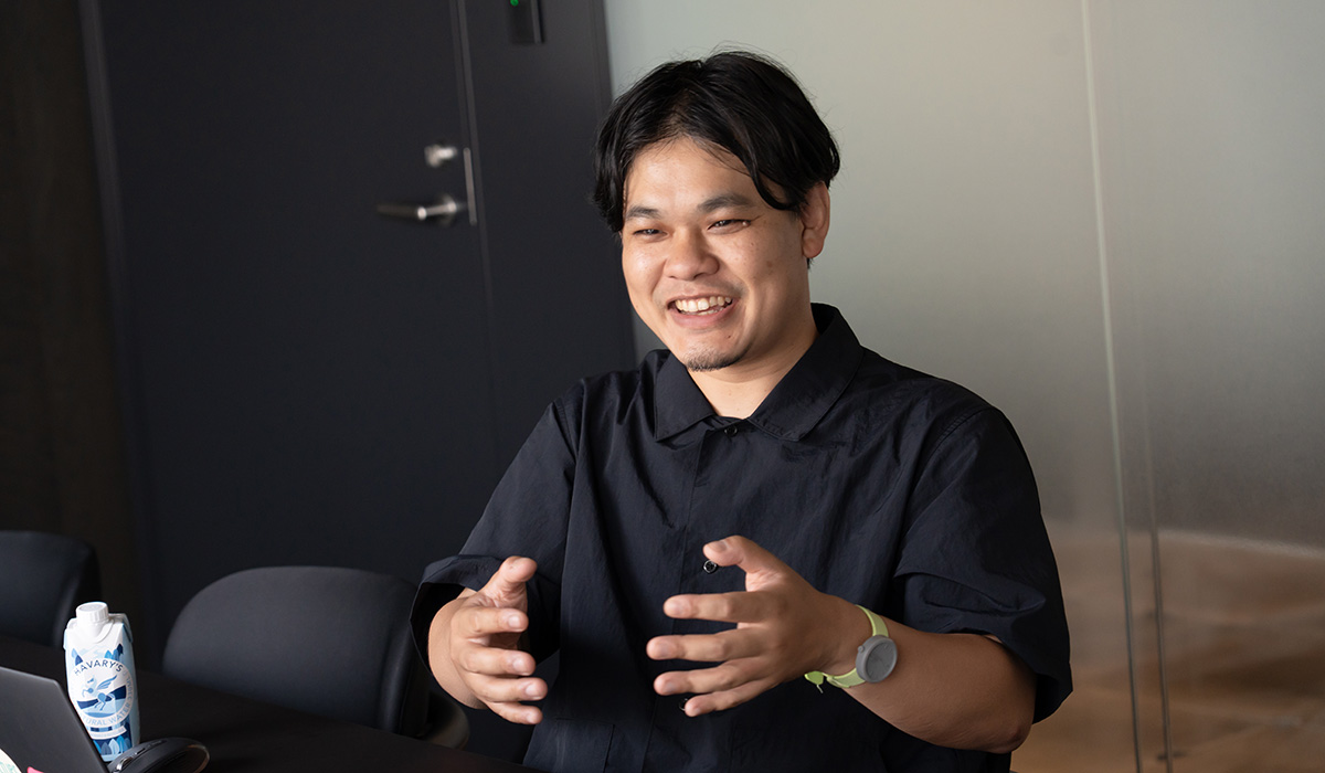 吉羽さんのバストショット。両手を前に出して広げるような仕草をしながら笑顔で話している様子