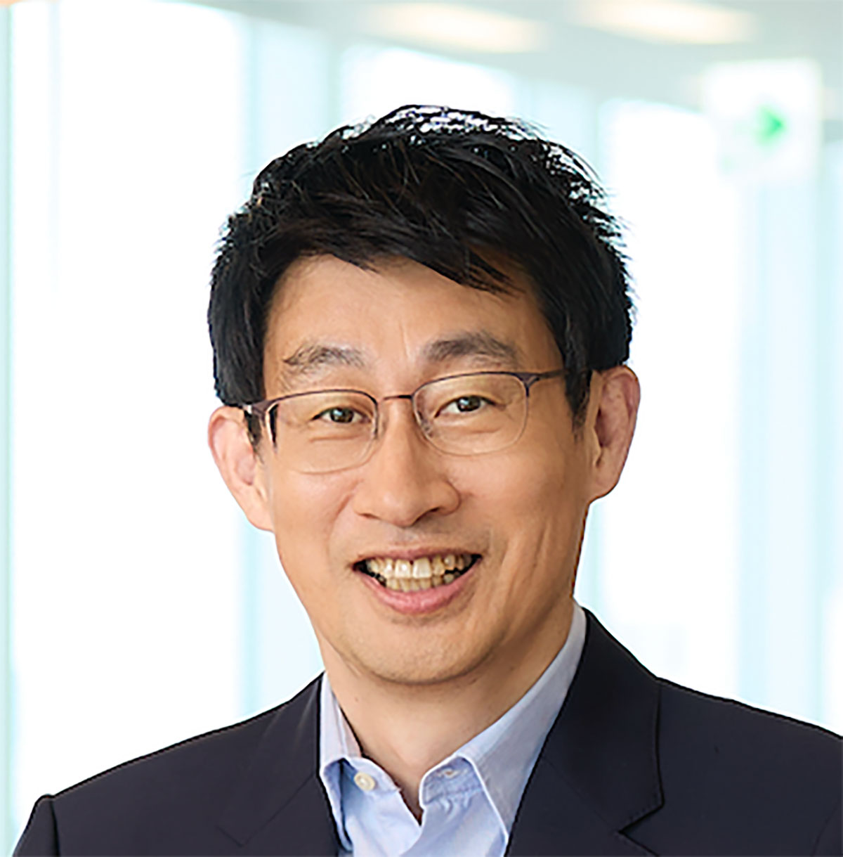 Shin, wearing glasses, is facing forward with a smile. The background is bright, evoking a business-like atmosphere.