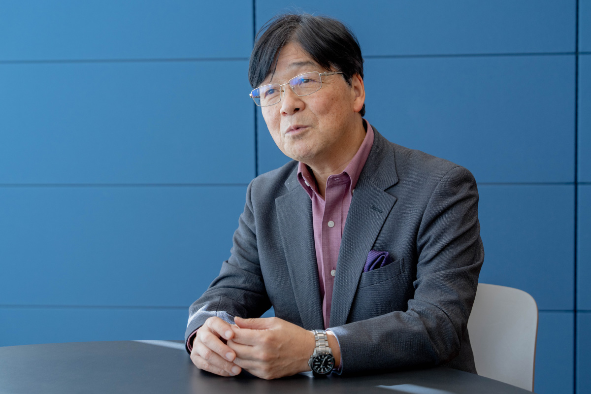 立正大学の西田先生の上半身ショット。両手を軽く組みながら前のテーブルに置き、話をしている様子。