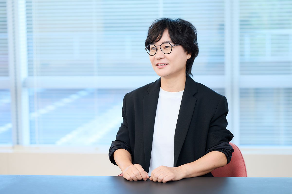 オフィスのテーブル席で、黒いジャケットを着た朴イビンが椅子に座り、前方を見ながら話している写真。