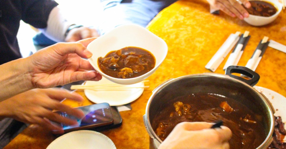 テーブルを囲む参加者が、鍋から鹿肉のシチューを器に取り分けている様子