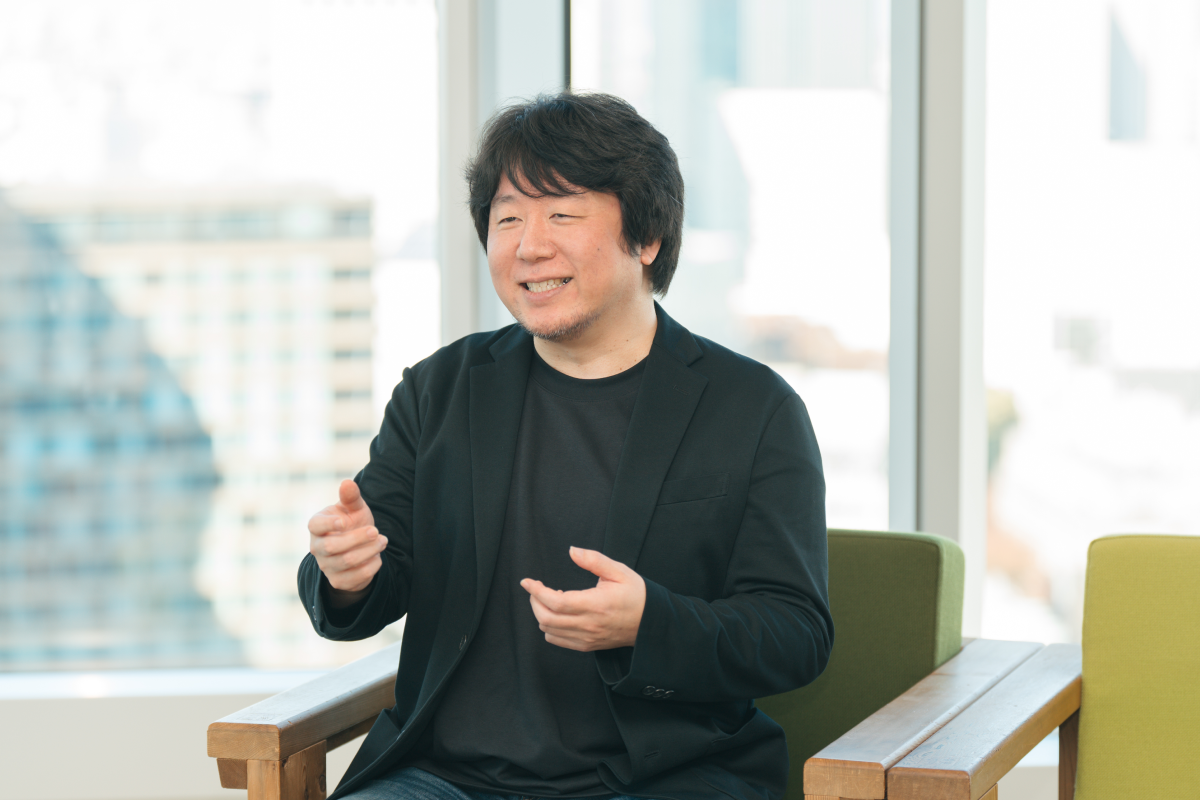 冨川が椅子に座り、笑顔で両手を使って話している様子。