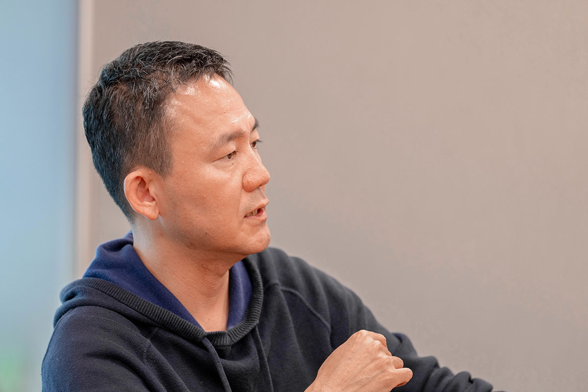 横向きで話す出前館CEOの上半身写真。短く整えた髪にネイビーのパーカーを着て、腕を曲げながら真剣な表情で会話している。