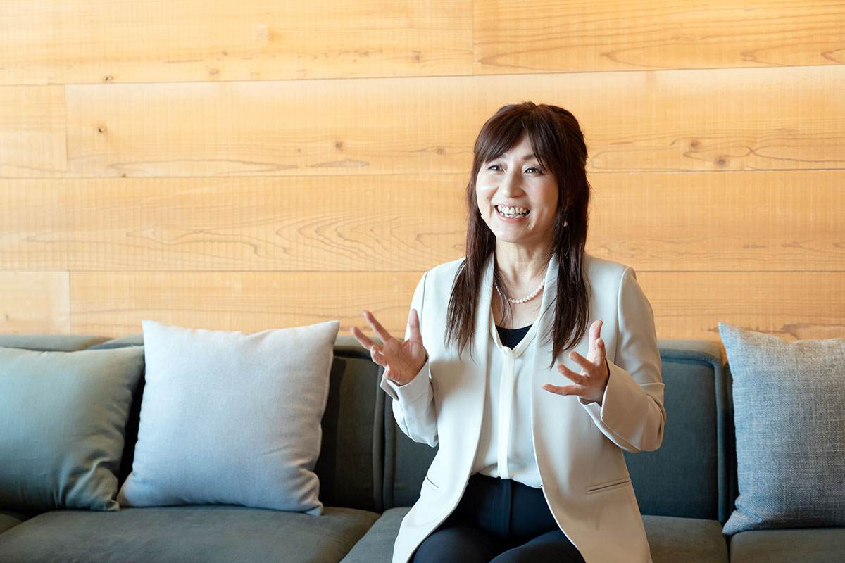 ソファに座った女性・正木CEOが笑顔で話しています。木目の壁を背景に、リラックスした雰囲気が漂っています。
