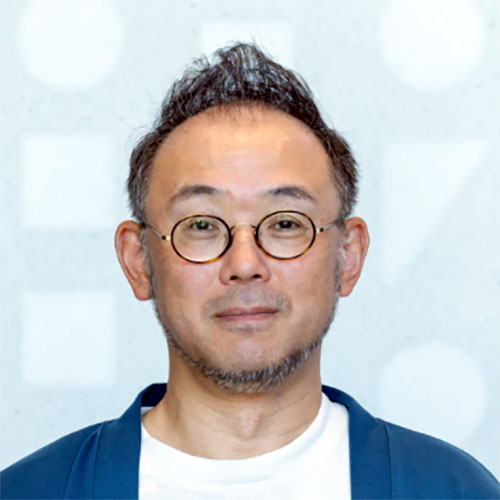 丸眼鏡をかけた澤田CEOが正面を向いているバストショット。髪は短く立ち上がり、青色の羽織のような服を着ている。背景は淡い幾何学模様