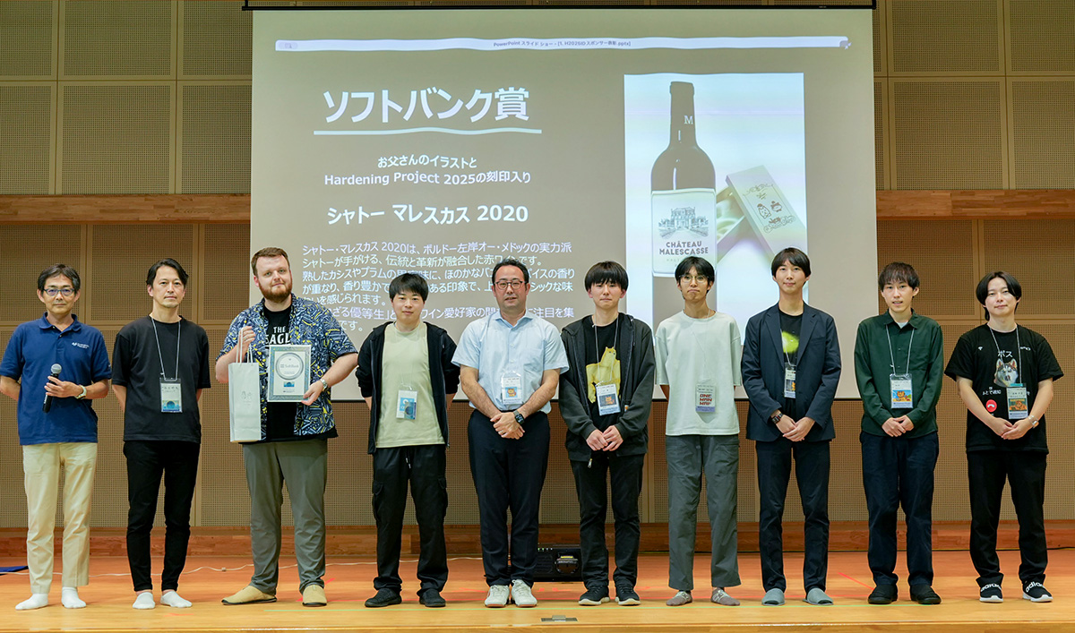 ステージ上に9人の男女が横一列に並び、記念撮影をしている様子。中央のスクリーンには「ソフトバンク賞」「Hardening Project 2025の刻印入り」「シャトー マレスカス 2020」と書かれ、ワインボトルと木箱の写真が映し出されている。