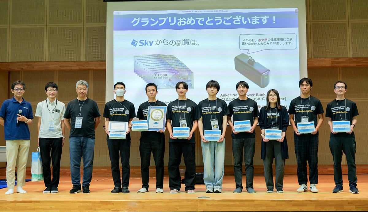 ステージ上で11人の人々が横一列に並び、記念撮影をしている様子。中央のスクリーンには「グランプリおめでとうございます！」「Skyからの副賞は」と表示され、1,000円分のギフトカードの束と「Anker Nano Power Bank」の画像が映し出されている。
