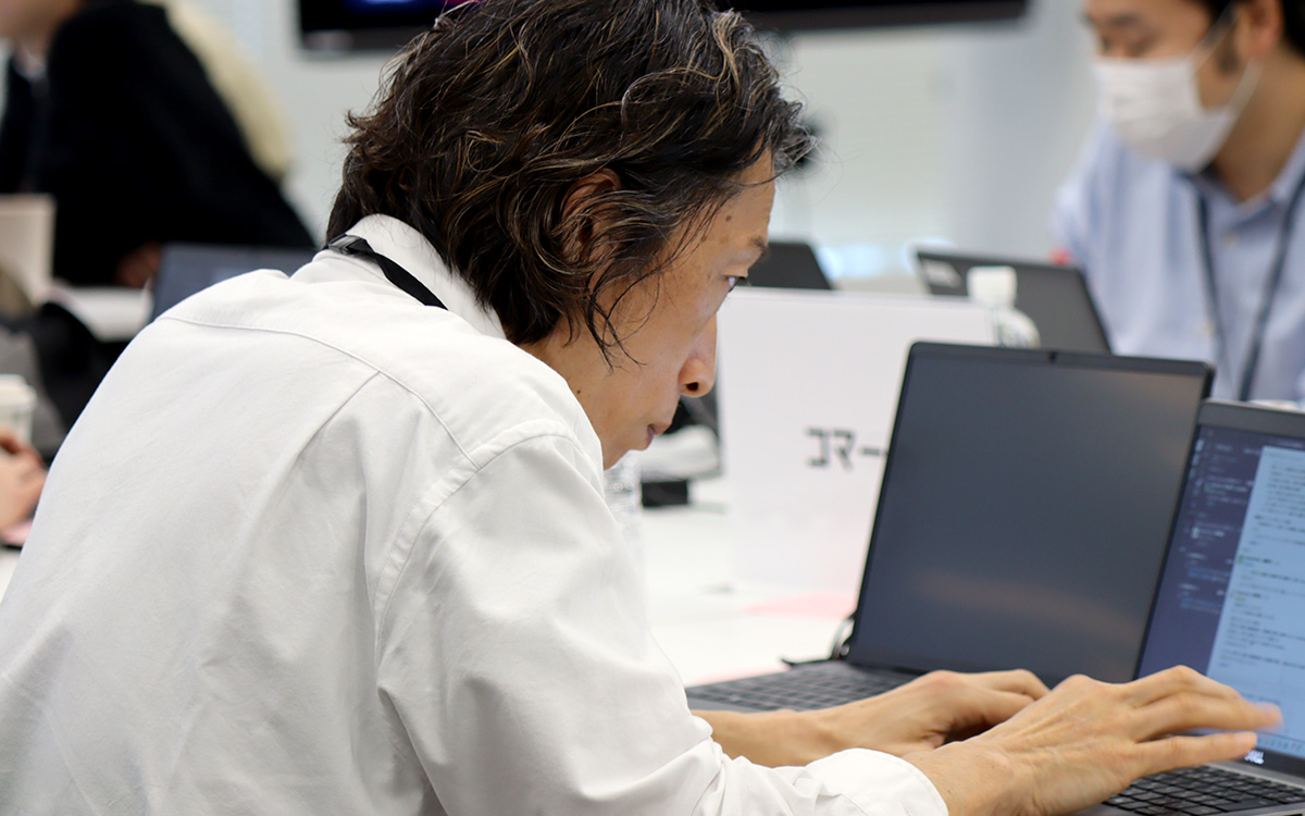 会議室で男性がノートパソコンを操作している様子。男性は白いシャツを着て、画面に顔を近づけるようにして真剣な表情でキーボードを打っている。