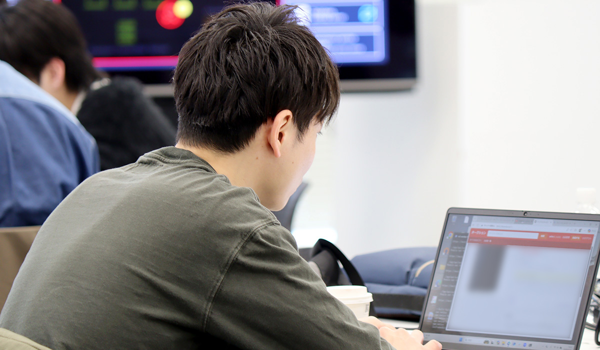 室内の作業スペースで男性がノートパソコンを操作している後ろ姿。