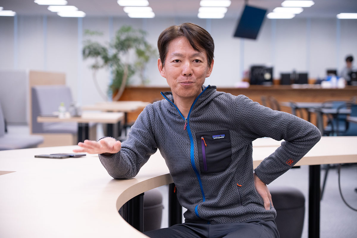 榊社長が片手を前に伸ばし、もう片方の手を腰に当てて話しています。