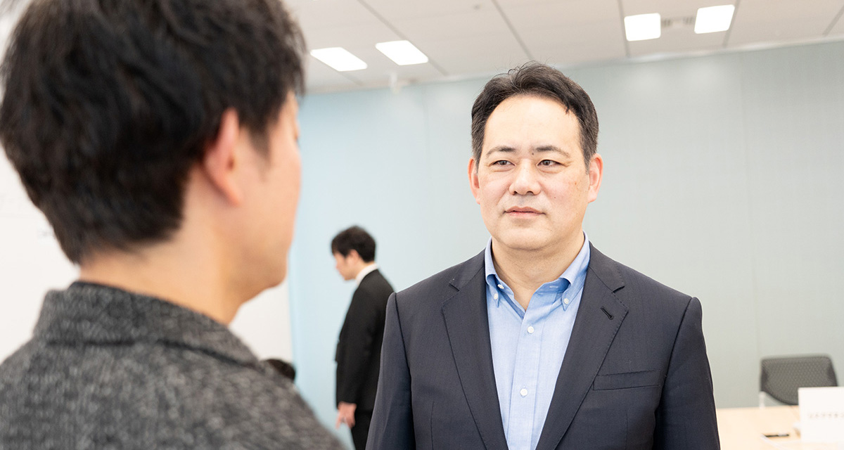 スーツ姿の男性が、別の男性と向かい合い、真剣な表情で会話をしています。